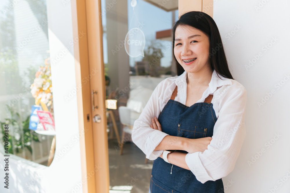 一名亚洲妇女在经营一家小店时双臂交叉，站在前面微笑