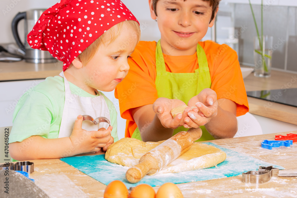 Two kids roll dough and cut shapes on the kitchen