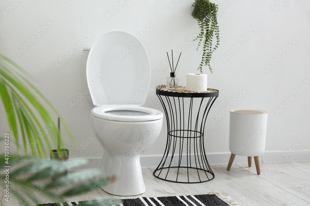 Toilet bowl, table with bathroom accessories and bin near white wall