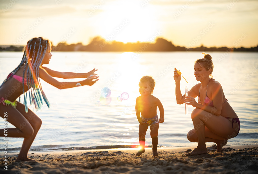 Brother and sister play with their mom blowing bubbles on the lake