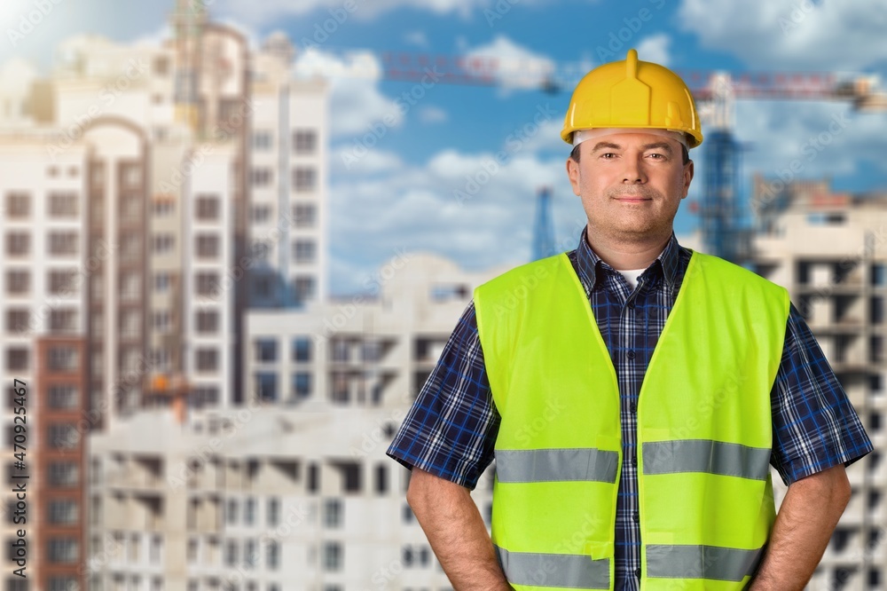 Male construction site manager standing wearing safety helmet, thinking