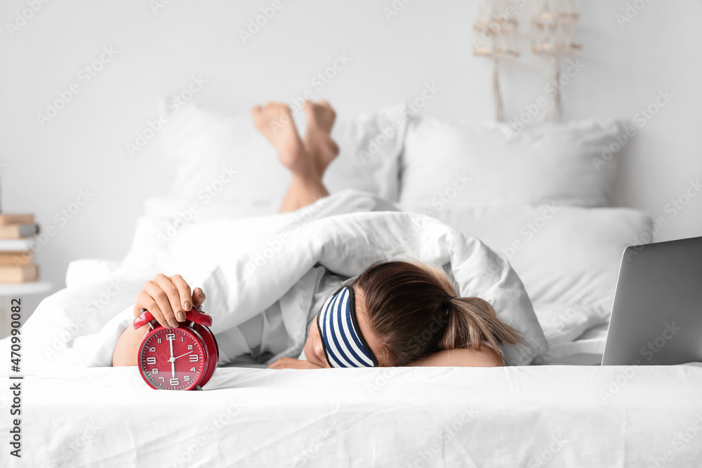 Morning of young woman with alarm clock sleeping in bed