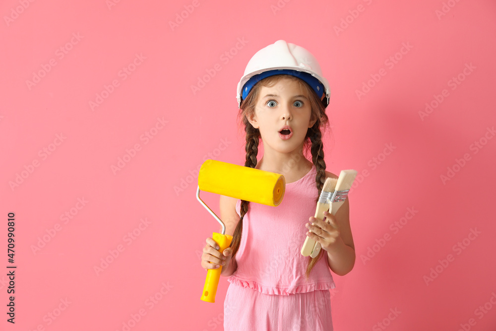 Surprised little girl with paint roller and brushes on pink background