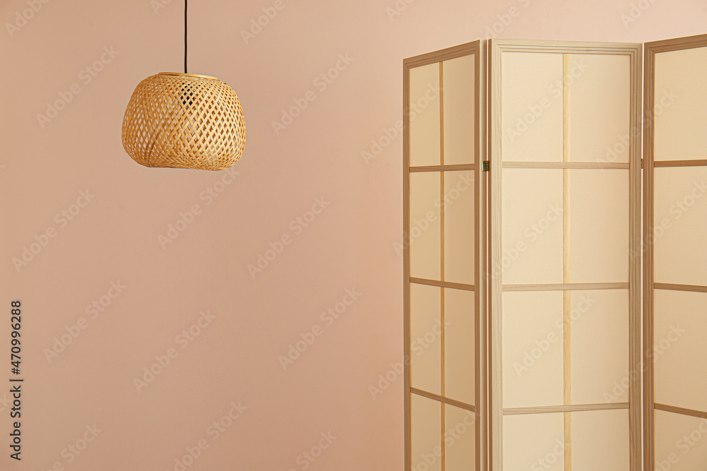 Stylish folding screen and wicker lamp on wall background