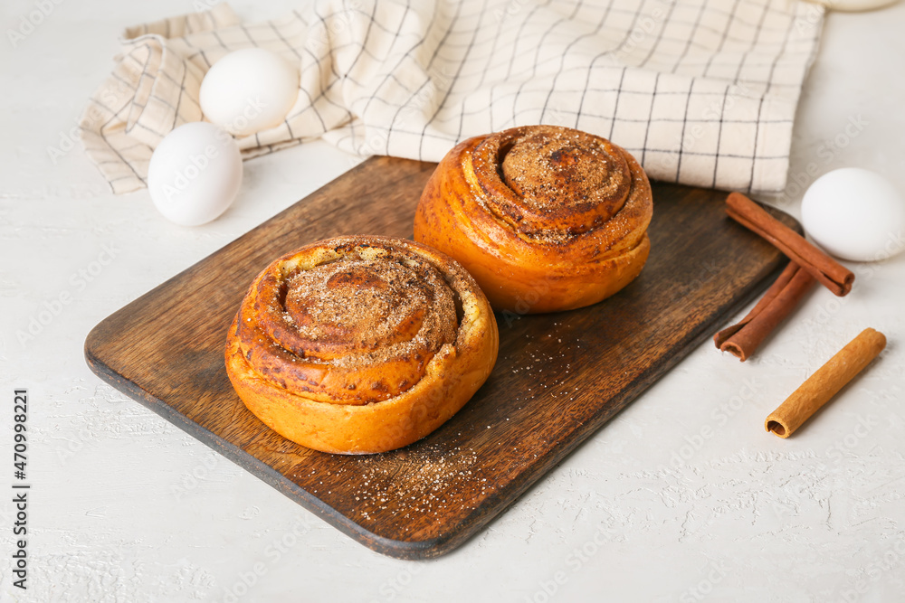 Wooden board with tasty cinnamon rolls on white background