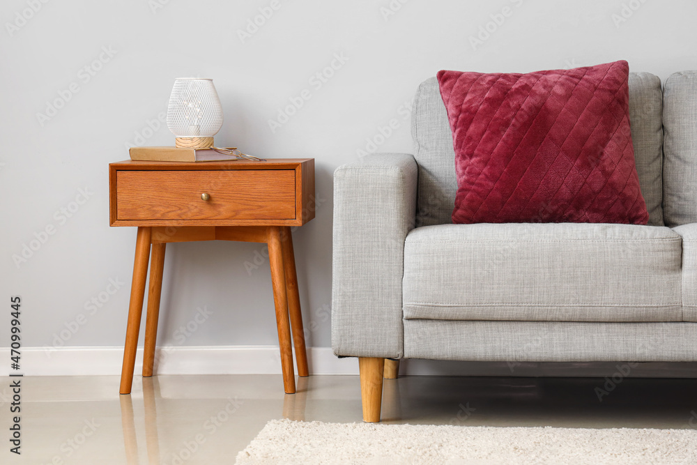 Stylish interior with wooden bedside table and couch near light grey wall