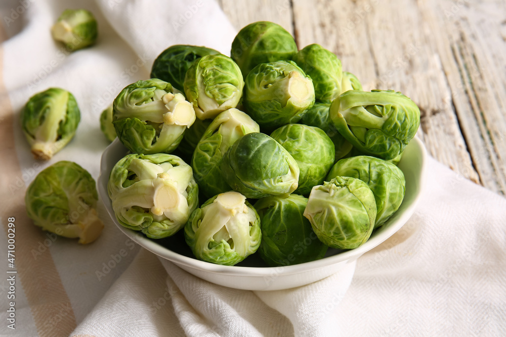 Bowl with fresh raw Brussels cabbage on light wooden background, closeup