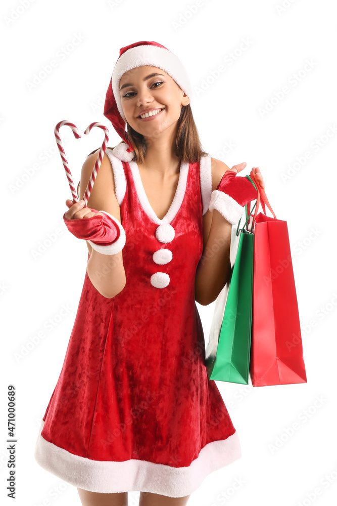 Beautiful woman in Santa costume, with candy canes and shopping bags on white background