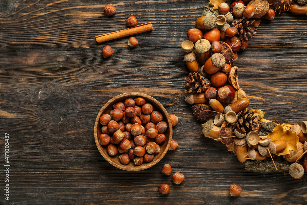 Bowl with hazelnuts and beautiful acorn wreath on wooden background