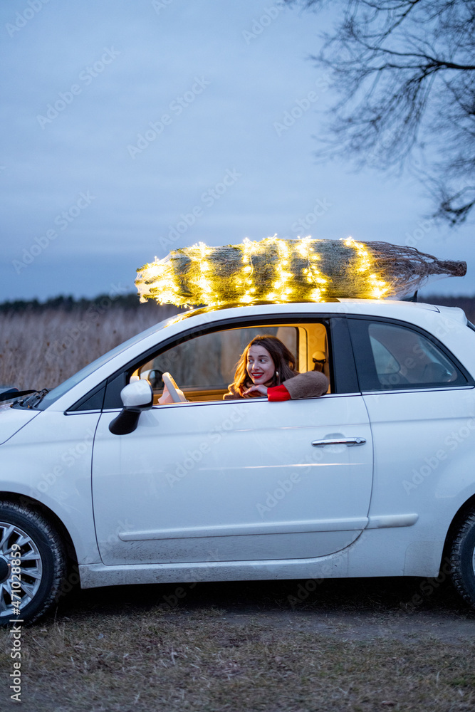 Woman driving car with a illuminated Christmas tree on a rooftop. Concept of New Year preparation. I