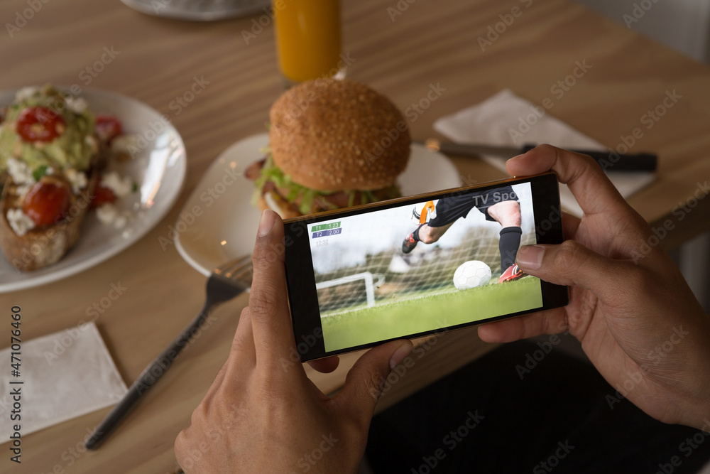 Hands of african american man at restaurant watching soccer match on smartphone