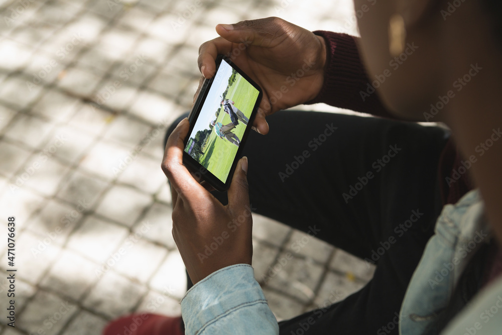 African american man in park watching golf match on smartphone