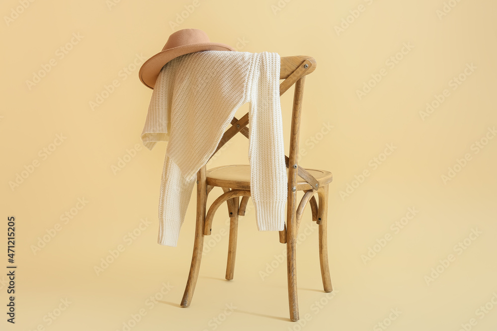 Stylish winter clothes on chair against color background