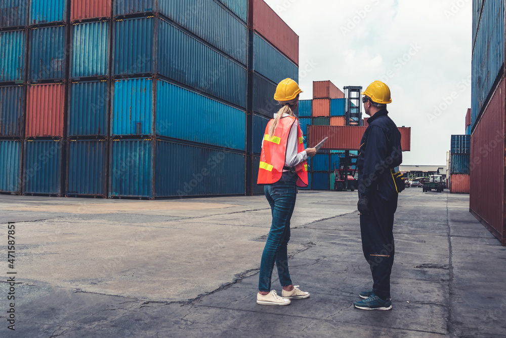 Industrial worker works with co-worker at overseas shipping container yard . Logistics supply chain 