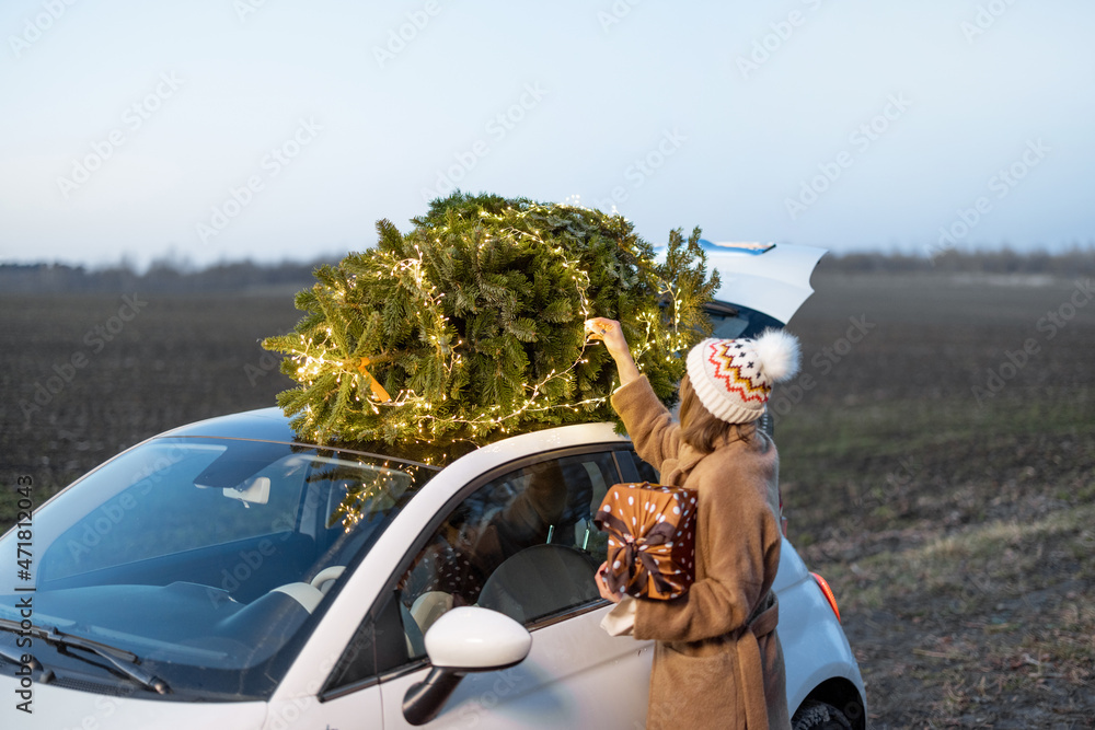 Woman packing Christmas tree on a rooftop of her car, getting ready for a holidays. Idea of Christma