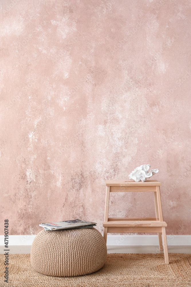 Wooden step stool and pouf with magazines near pink wall