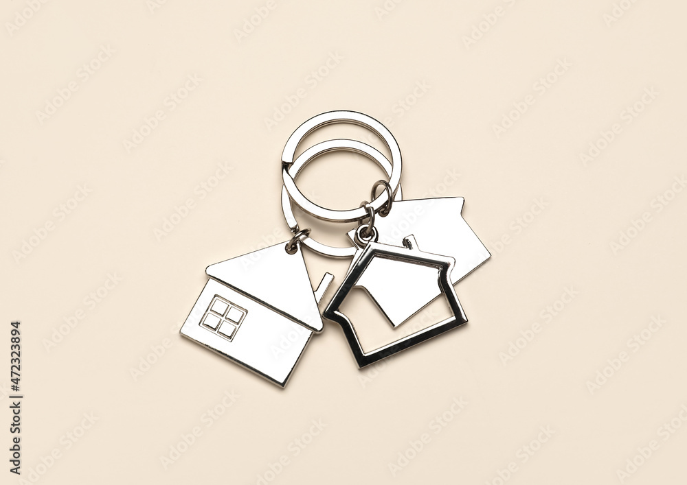 Silver house shaped keychains with keyrings on beige background