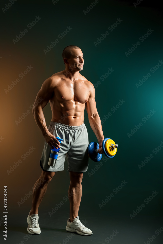 Male bodybuilder with protein shake and dumbbell on dark background