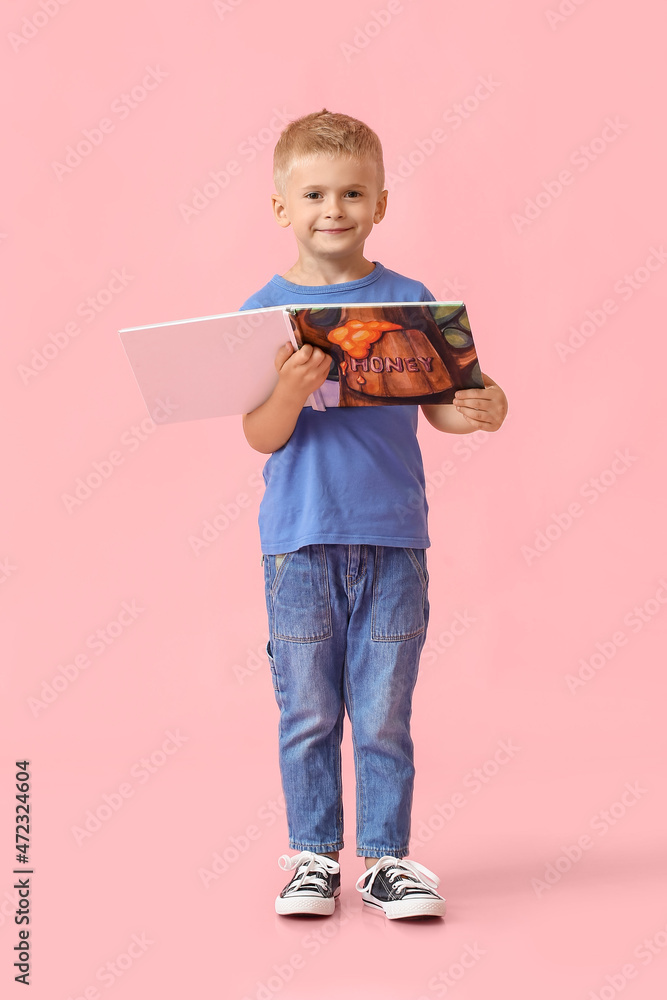 Adorable little boy with book on pink background