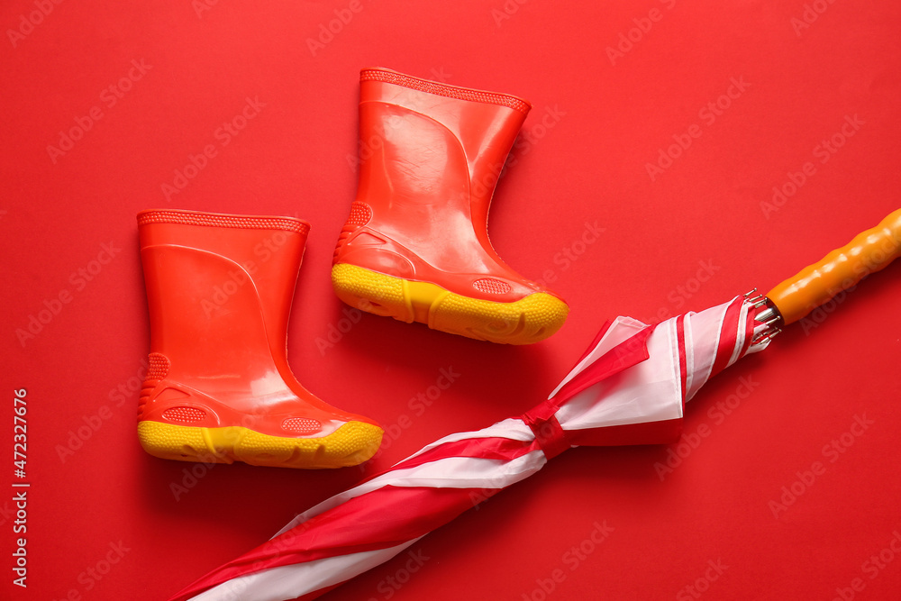 Pair of rubber boots and umbrella on red background, closeup