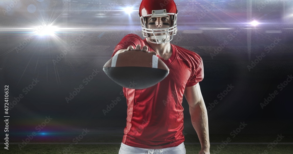 Portrait of confident male american football player offering ball at illuminated sports field