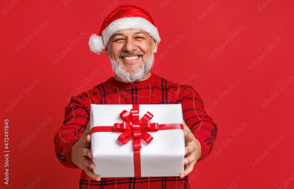 cheerful surprised   senior  man  with red Santa hat  holds a Christmas gift and laughing a colored 