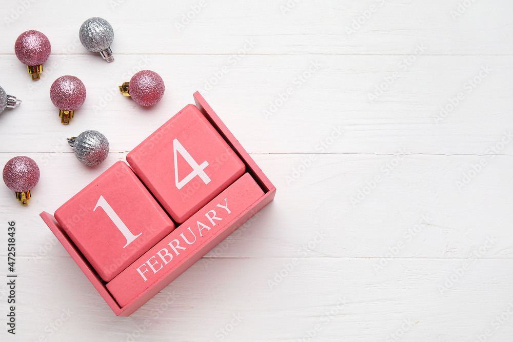 Calendar with date of Valentines Day and Christmas balls on light wooden background