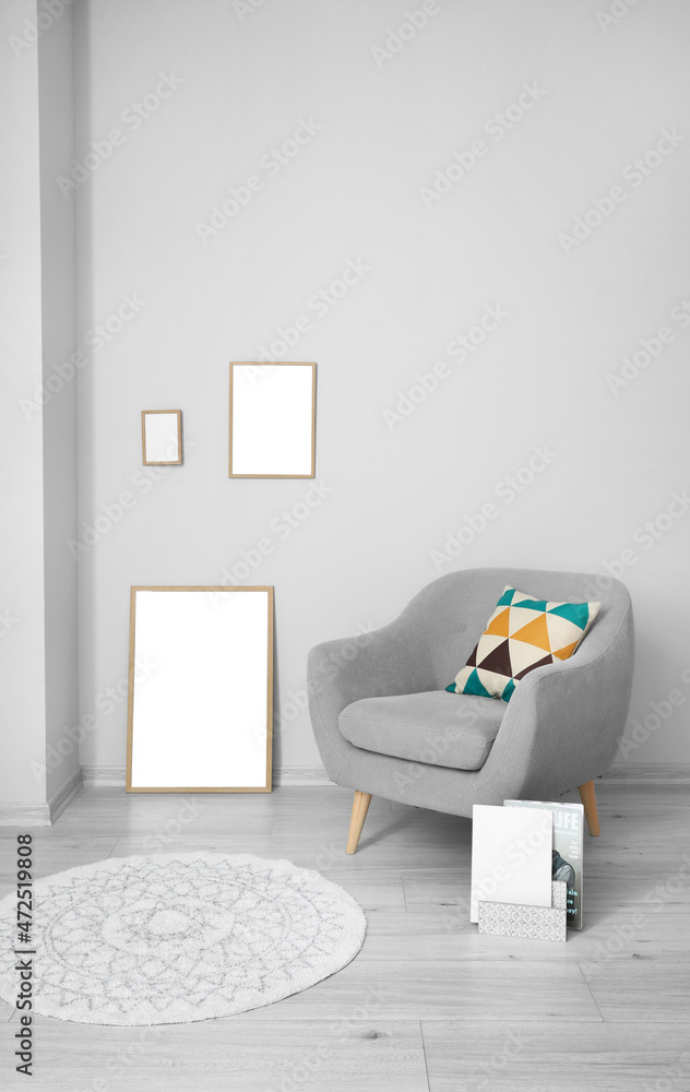 Blank frames and grey armchair near light wall