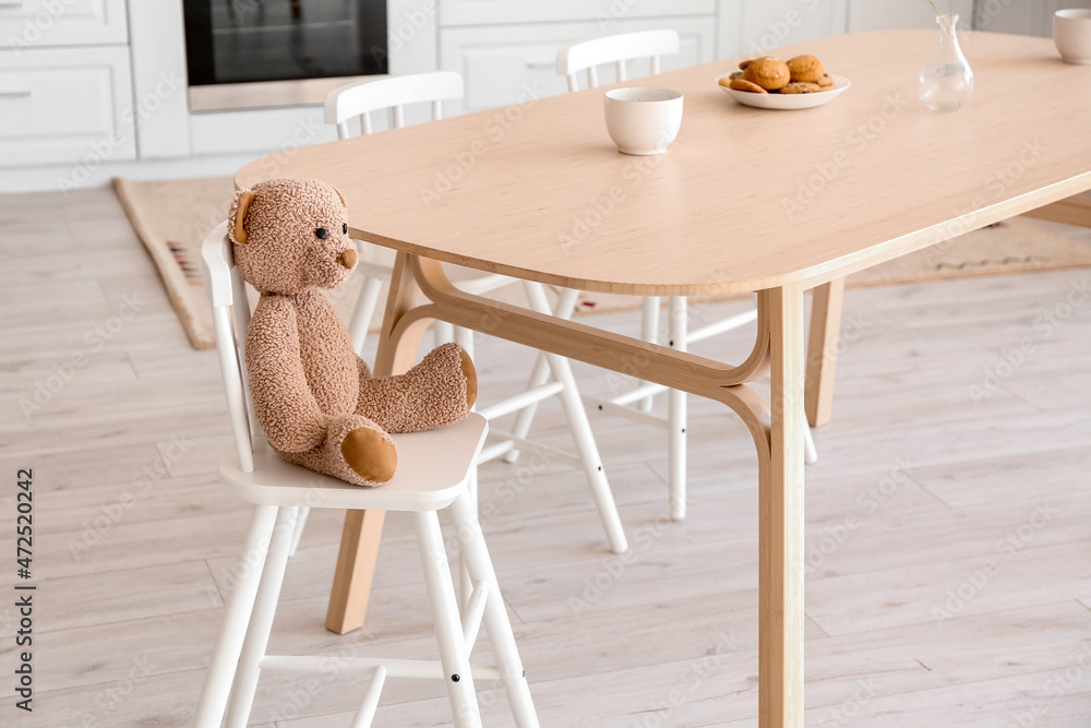 Chair for baby with toy bear near table in modern kitchen