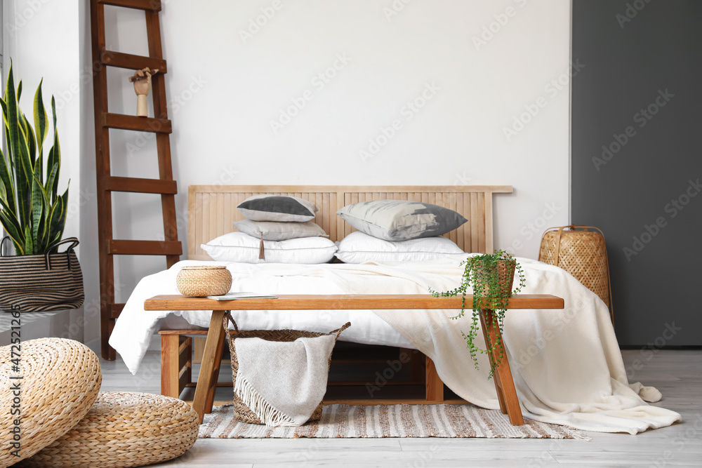 Wooden bench with basket and houseplant in interior of light bedroom