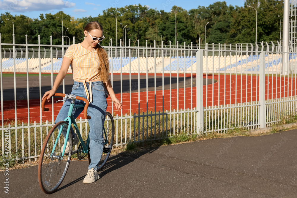 Pretty teenage girl in sunglasses with bicycle near stadium