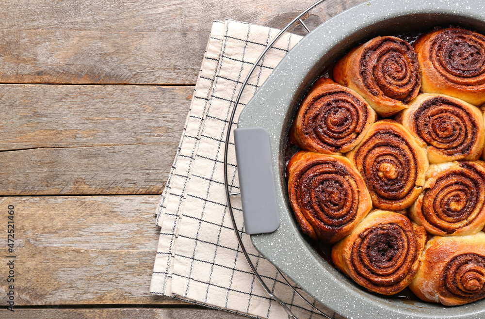 Baking dish with tasty cinnamon rolls on wooden background, closeup