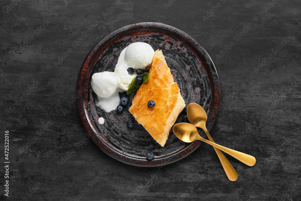 Plate with piece of tasty apple strudel on black background