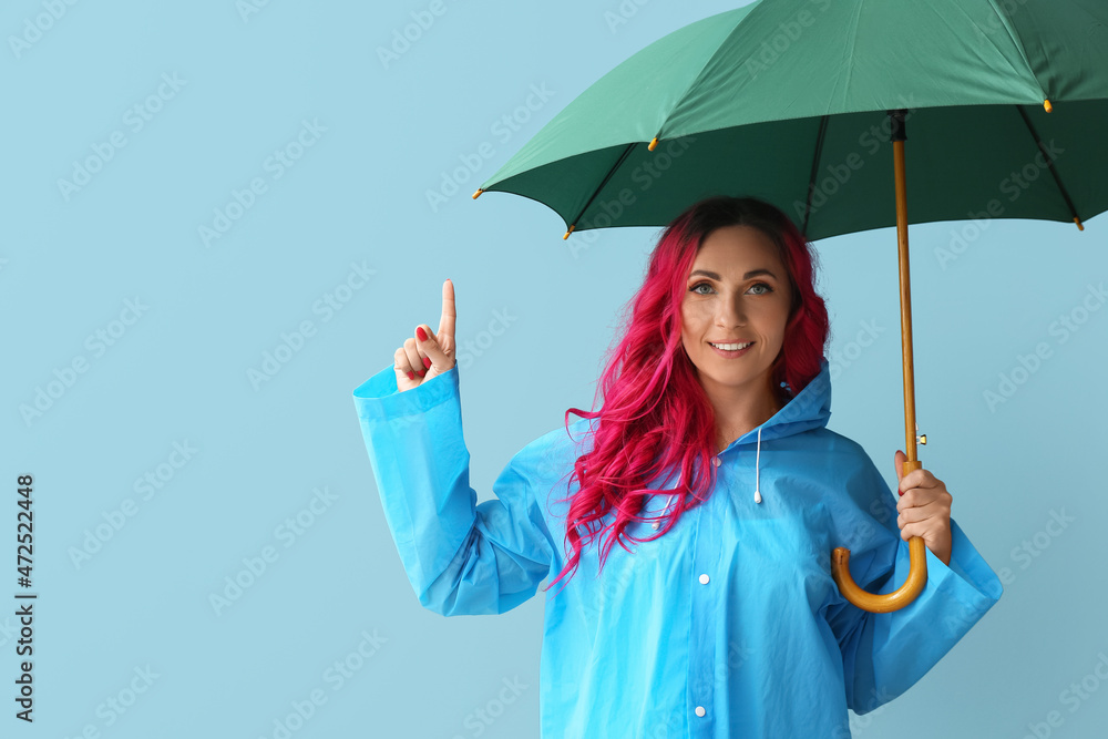 Beautiful woman in raincoat and with umbrella on color background