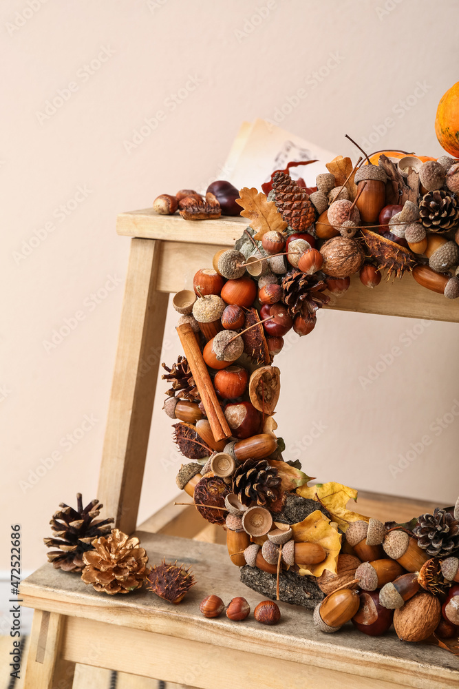 Beautiful acorn wreath on step ladder near light wall, closeup