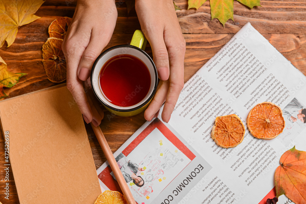 Woman with cup of tea, notebook, newspaper, dried lemon slices and fallen leaves on wooden backgroun