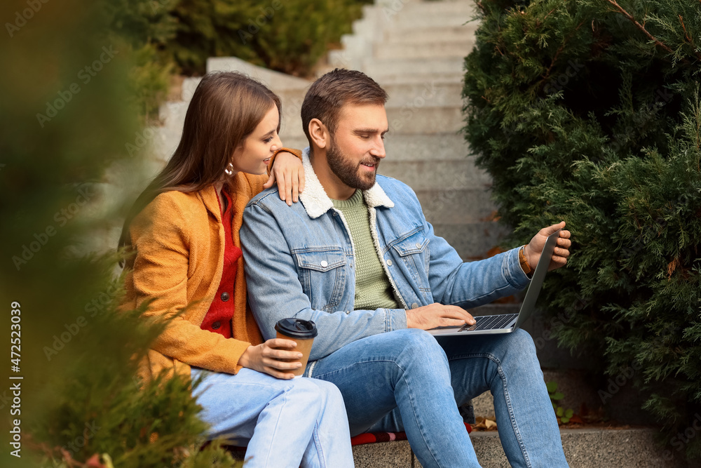 Couple sitting on stairs and using laptop in autumn park