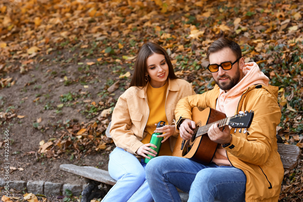 Young man playing guitar for his girlfriend in autumn park