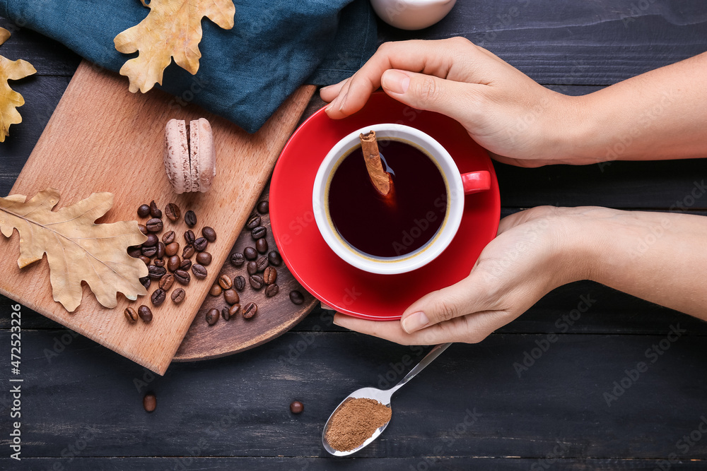 Female hands with cup of tasty coffee, cinnamon and beans on black wooden background