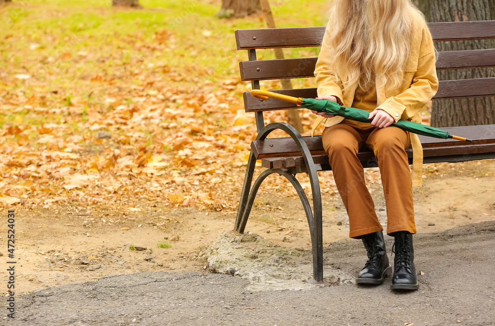 Young woman sitting on bench with stylish bright umbrella in autumn park, closeup