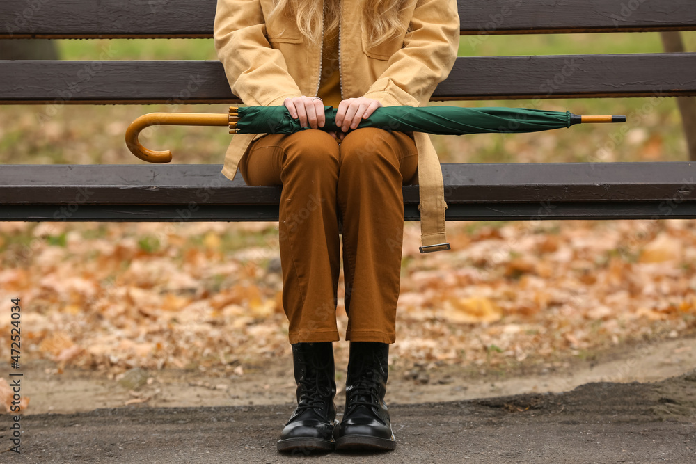 Young woman sitting on bench with stylish bright umbrella in autumn park, closeup