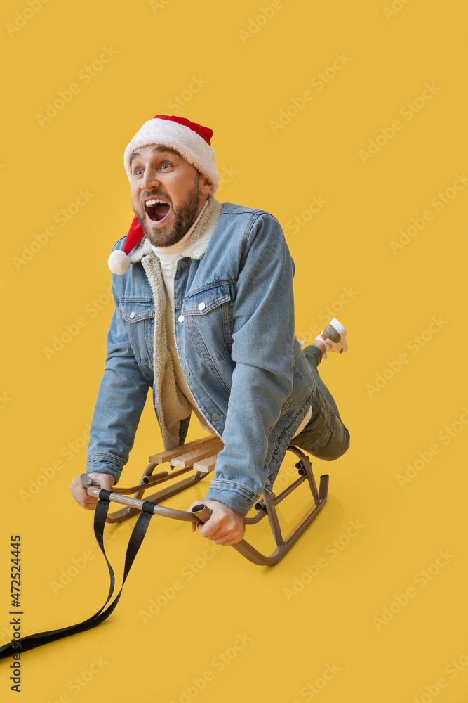 Young sledding man in Santa hat on color background