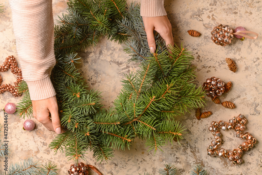 Woman making Christmas wreath with fir branches on beige background