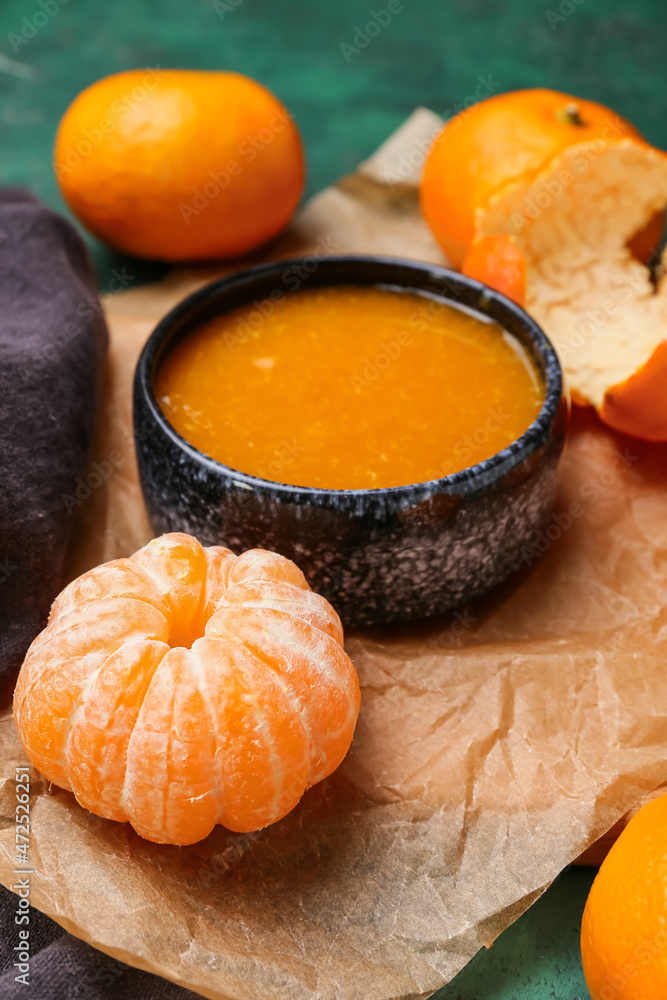 Parchment with bowl of tasty tangerine jam on table, closeup