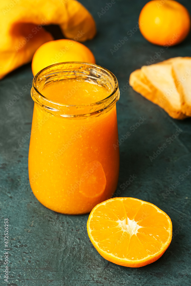 Jar of tasty tangerine jam on dark background