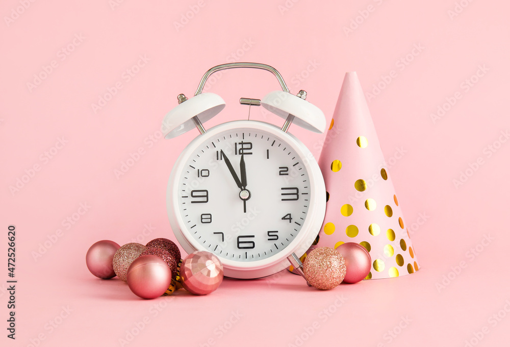 Alarm clock, party hat and Christmas balls on pink background