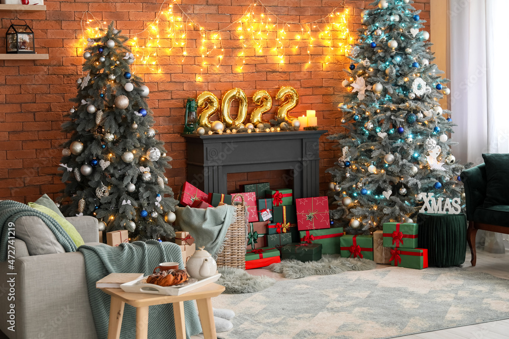 Interior of festive living room with Christmas trees, decorative mantelpiece and gift boxes