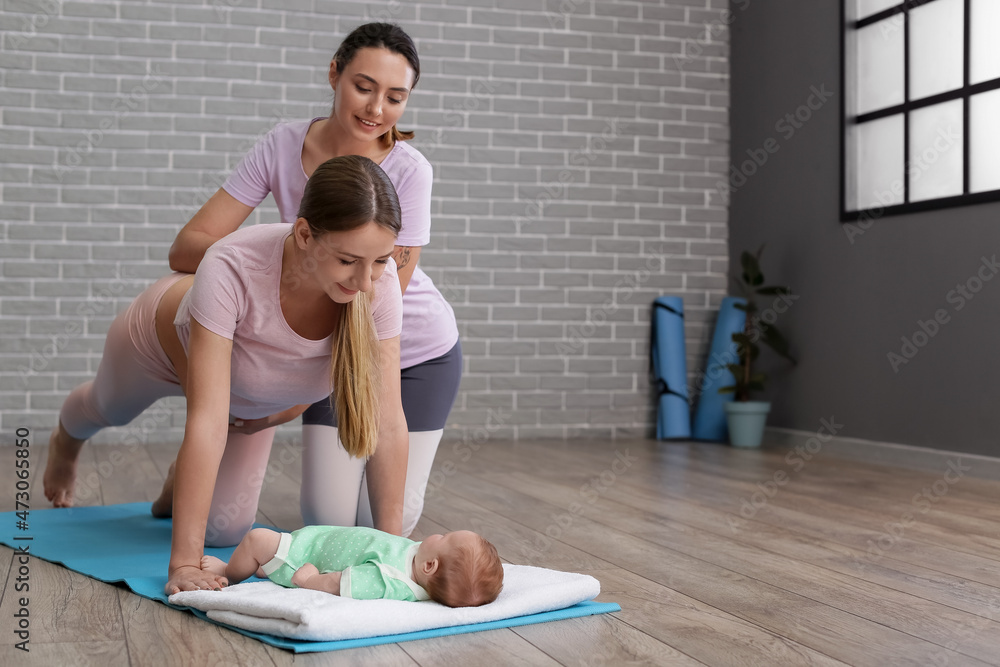 Young pregnant woman practicing yoga with little baby and trainer at gym