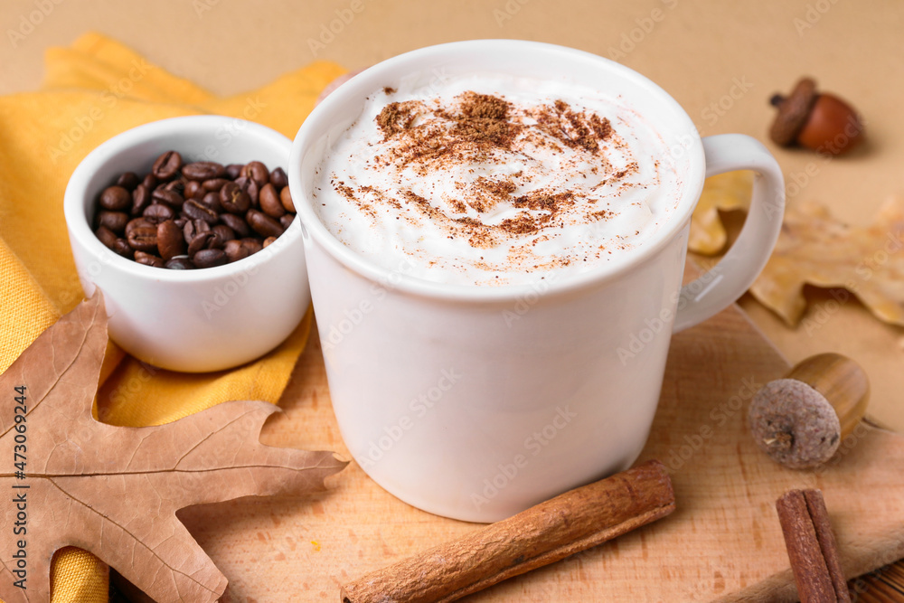 Cup of tasty coffee with cinnamon and beans on beige background