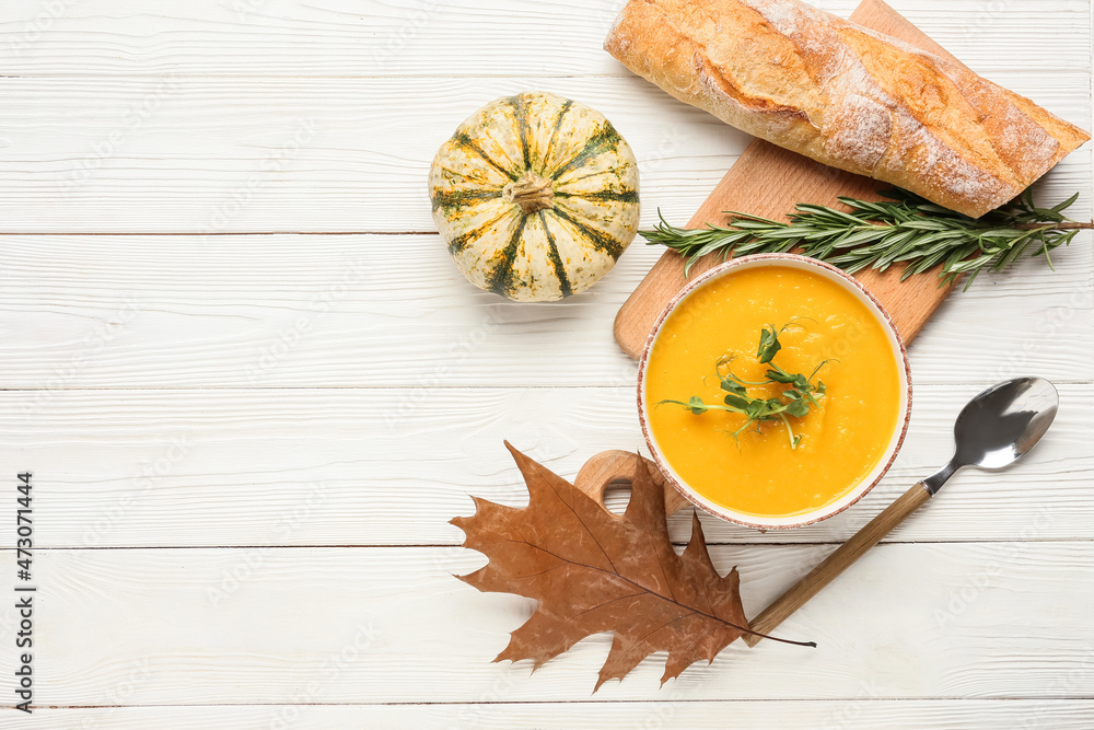 Bowl of pumpkin cream soup and bread on white wooden background